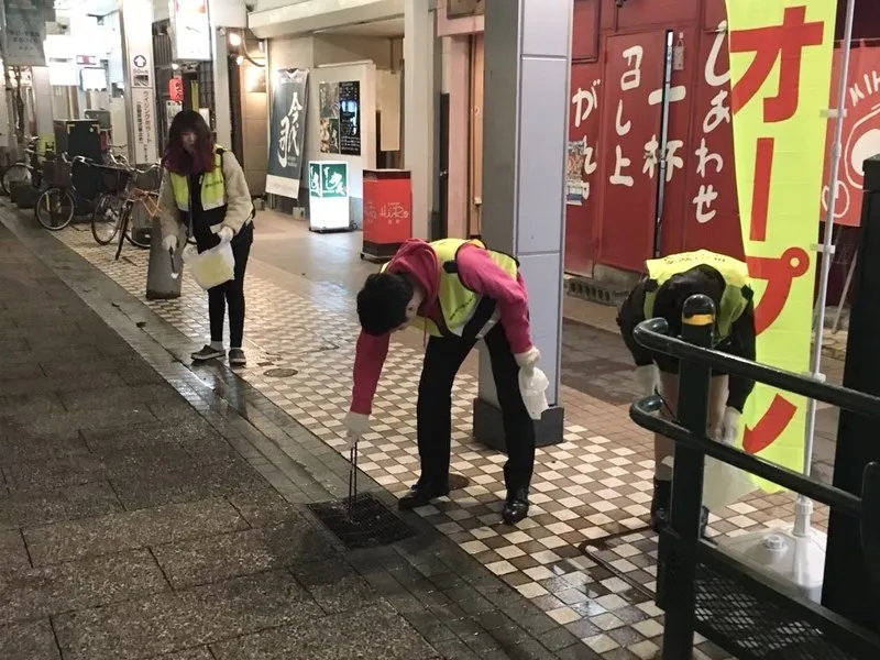 反射ベストを着た参加者が、歩道のごみをトングで拾っている