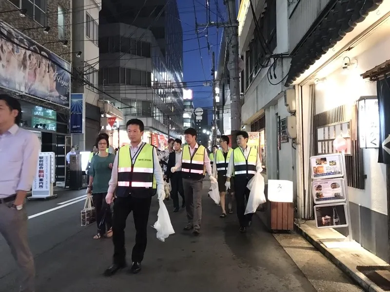 反射ベストを着た参加者が、ごみ袋を持って夜の街を歩いている